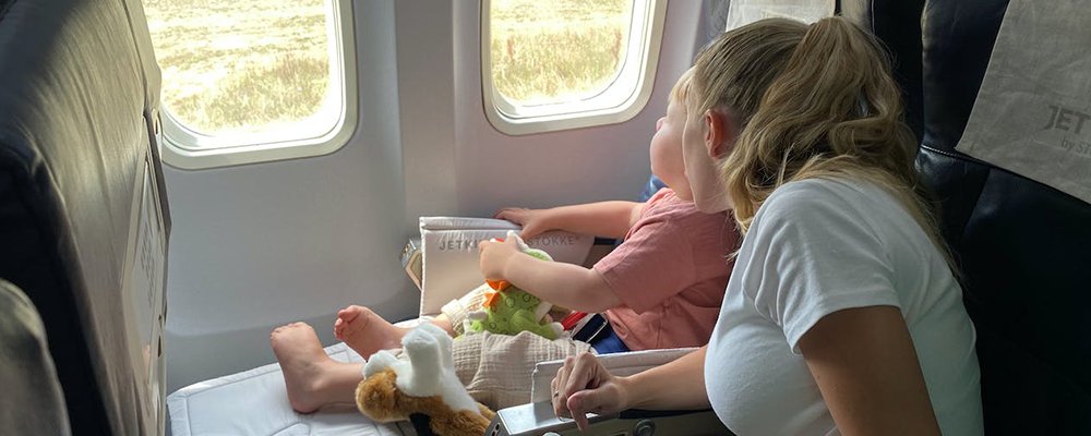 7 Ways To Take The Stress Out Of Flying With Children - The Wise Traveller - Mom with kid looking at airplane window